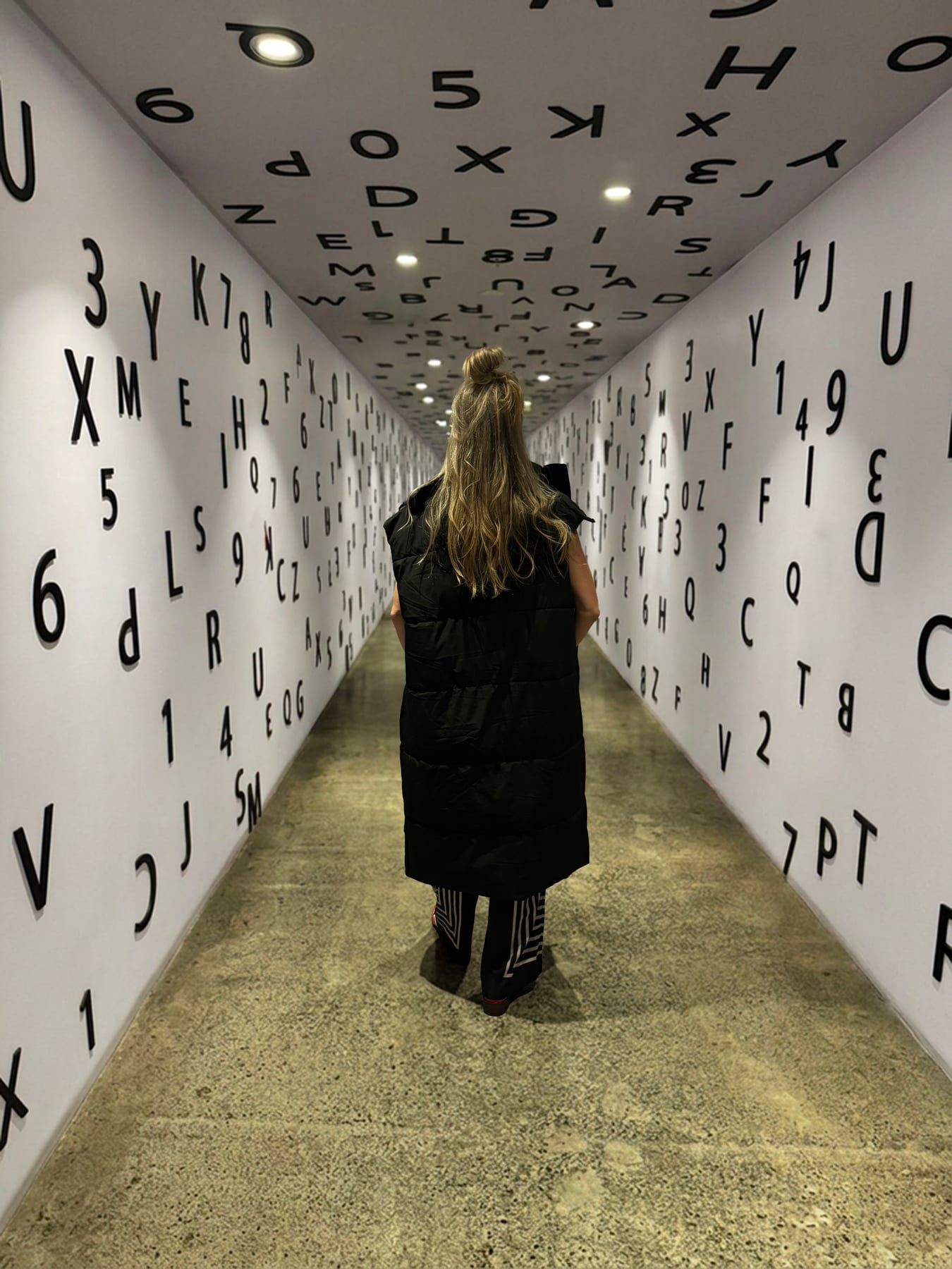 Janelle walking through a corridor covered with letters and numbers